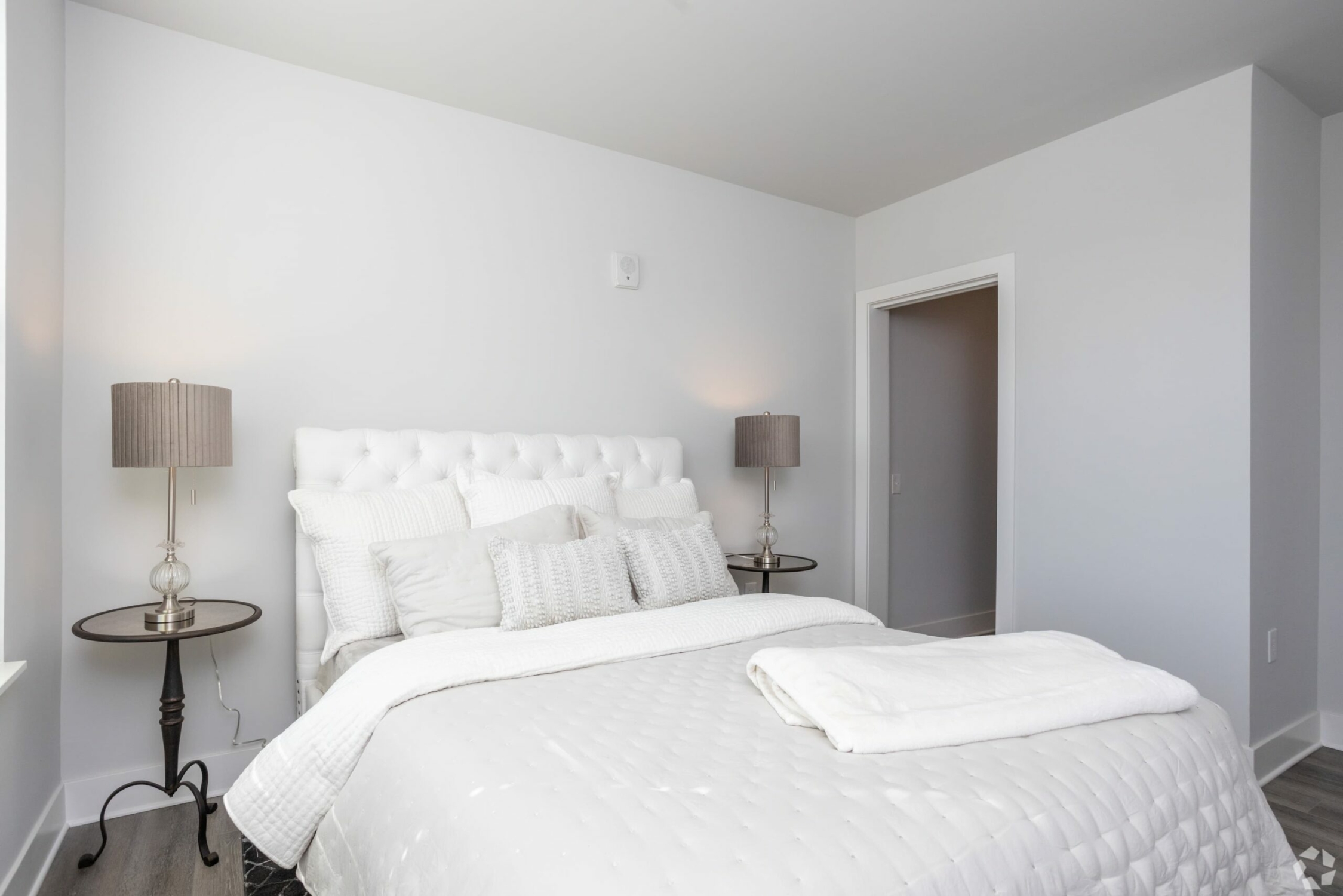 A white bed in a bedroom with hardwood floors.