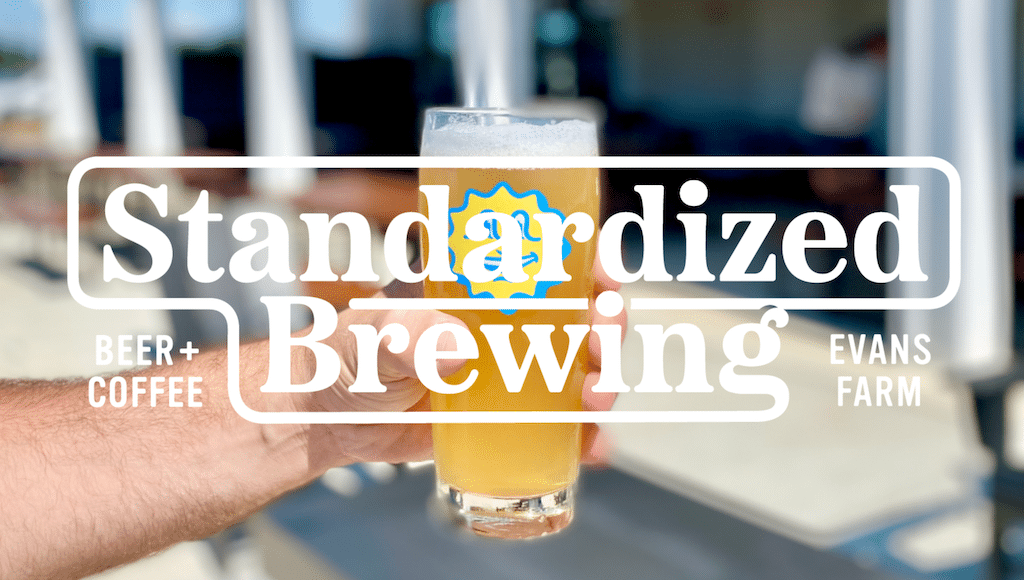 A hand holding a glass of beer with the logo for "Standardized Brewing" and "Beer + Coffee Evans Farm" overlayed on the image, highlighting a taste experience inspired by the vibrant Evans Farm neighborhood.