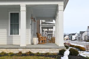 A front porch with two wooden rocking chairs and a small table overlooks a suburban street with snow patches on the ground.