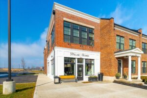 A two-story brick building with large windows houses the business "3 Pillar Homes." The entrance features a glass door, white trim, and a yellow bench outside.