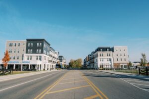 Wide street with marked lanes, lined by modern four-story apartment buildings on both sides under a clear blue sky.