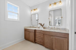 Modern bathroom with a double vanity, marble countertop, two mirrors, and gold light fixtures above each sink. A window provides natural light.