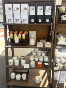Wooden display shelf at an outdoor market featuring fall-themed candles, wax melts, greeting cards, and pumpkin decorations with Halloween motifs.