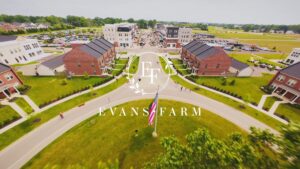 Aerial view of Evans Farm neighborhood featuring brick buildings, a central lawn with a flagpole, and a distant parking lot on a clear day.