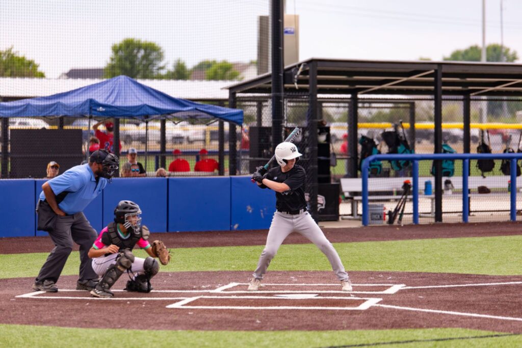 A baseball batter prepares to swing as the catcher and umpire crouch behind home plate on an outdoor field.