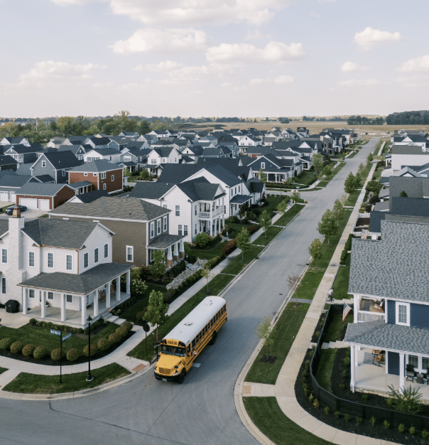 A yellow school bus drives down a residential street in OH, lined with modern suburban houses near Discover Evans Farm Location—ideal living in Lewis Center on a clear day.