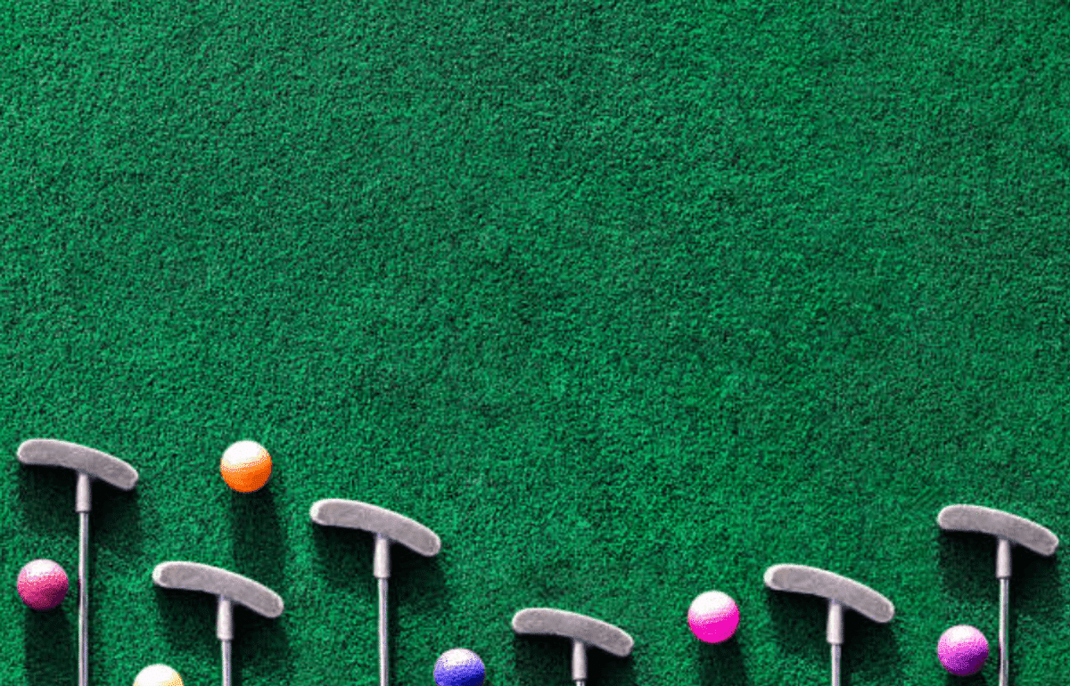 Mini golf putters and colorful golf balls are arranged on a green artificial turf surface, with most of the space showing the green texture.