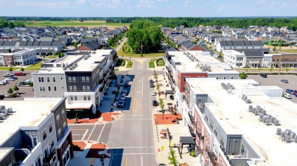 Aerial view of a suburban neighborhood with apartment buildings, parked cars, and tree-lined streets under a clear sky.