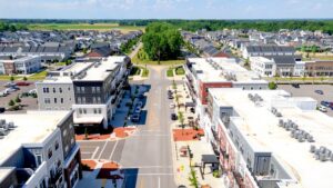 Aerial view of a suburban neighborhood with apartment buildings, parked cars, and tree-lined streets under a clear sky.