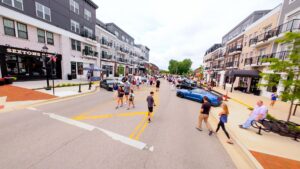 People walk along a closed city street lined with modern buildings and parked cars during a daytime outdoor event.