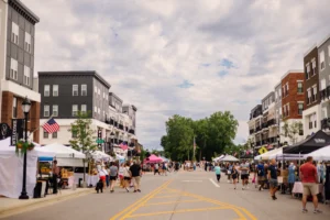 People walk along a closed street lined with vendor tents and shops during a community street fair on a cloudy day.