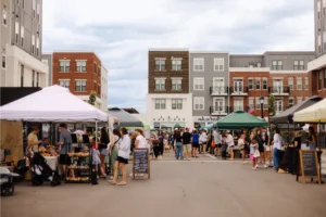 People browse vendor stalls at an outdoor market set up between apartment buildings on a cloudy day.