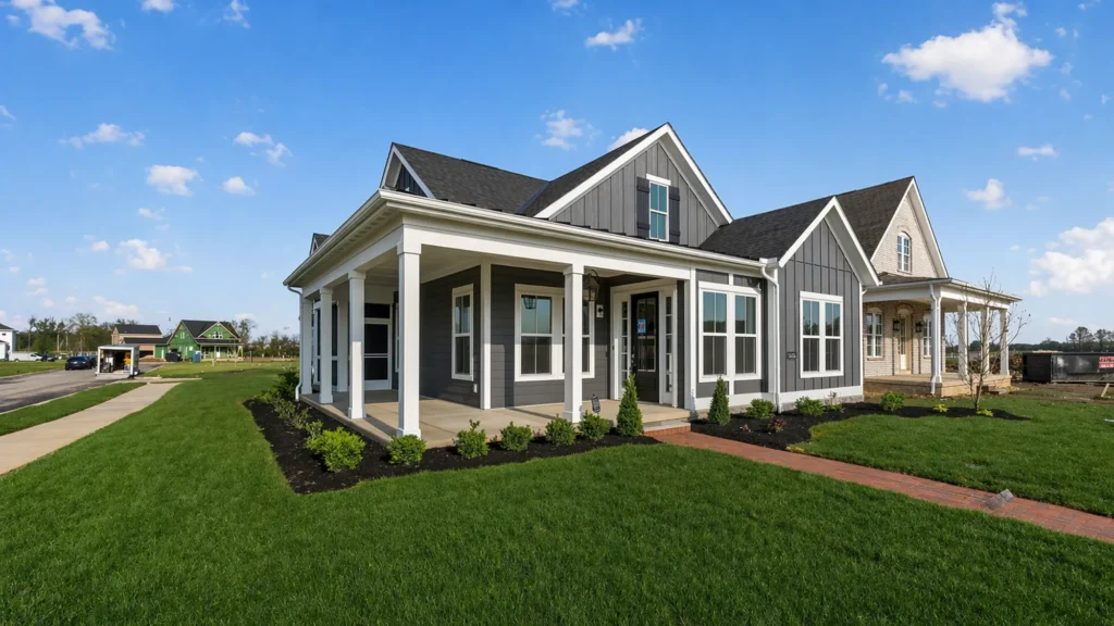 Modern gray house with white trim, large windows, and a wraparound porch, surrounded by a green lawn and landscaping on a sunny day—perfect for those looking to explore homeownership in Lewis Center.