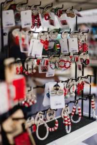 Earrings and bracelets with red, white, and black designs are displayed on a metal rack with tags and barcodes in a market or store setting.