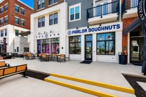 Street view of Parlor Doughnuts storefront with outdoor seating, adjacent to another business, on a clean, modern sidewalk with benches and yellow-painted steps.