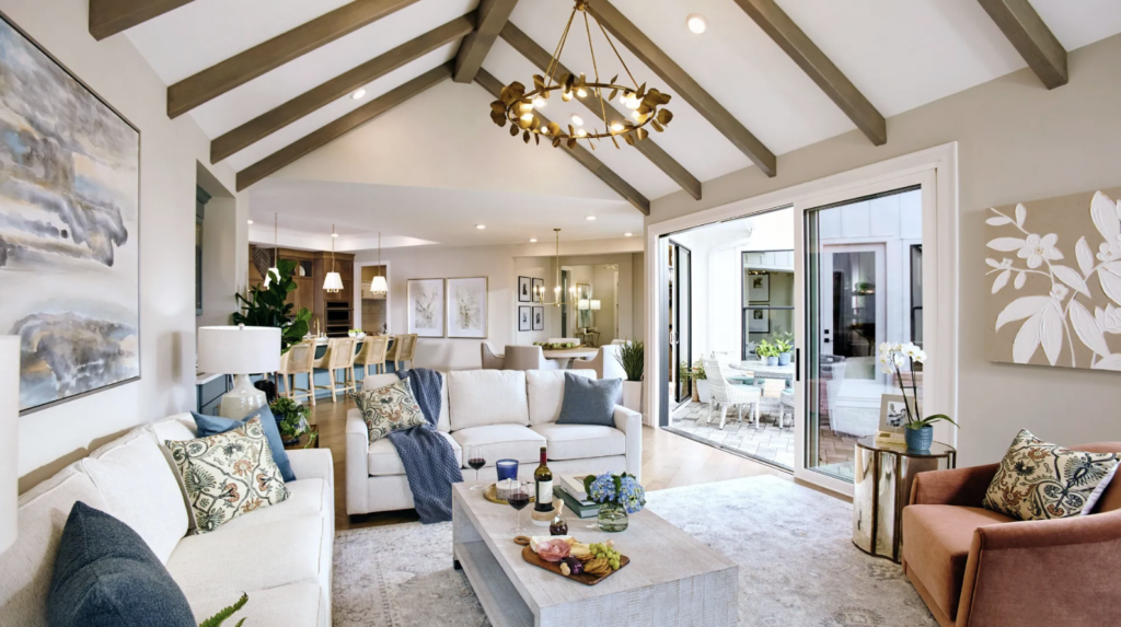 Spacious living room with vaulted ceiling, modern chandelier, two sofas, and a coffee table. Folding doors open to a bright patio. Neutral tones and decorative pillows add warmth—an inviting space to explore homeownership in Lewis Center.