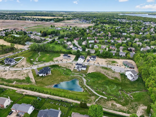Aerial view of a suburban neighborhood under development, with houses, roads, green spaces, and a small pond, surrounded by trees and fields—an inviting scene to explore homeownership in Lewis Center.