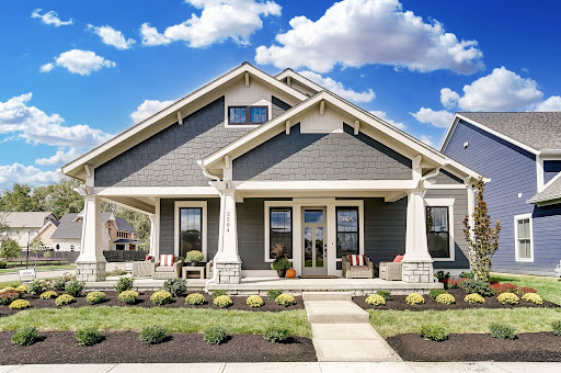 Single-story Craftsman-style house with gray siding, white trim, a covered front porch, two chairs, and landscaped yard under a blue sky with clouds—an ideal place to explore homeownership in Lewis Center.